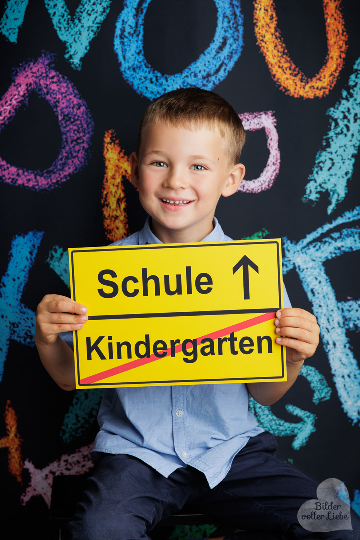 Junge Schulanfänger vor Einschulungskulisse mit bunten Requisiten